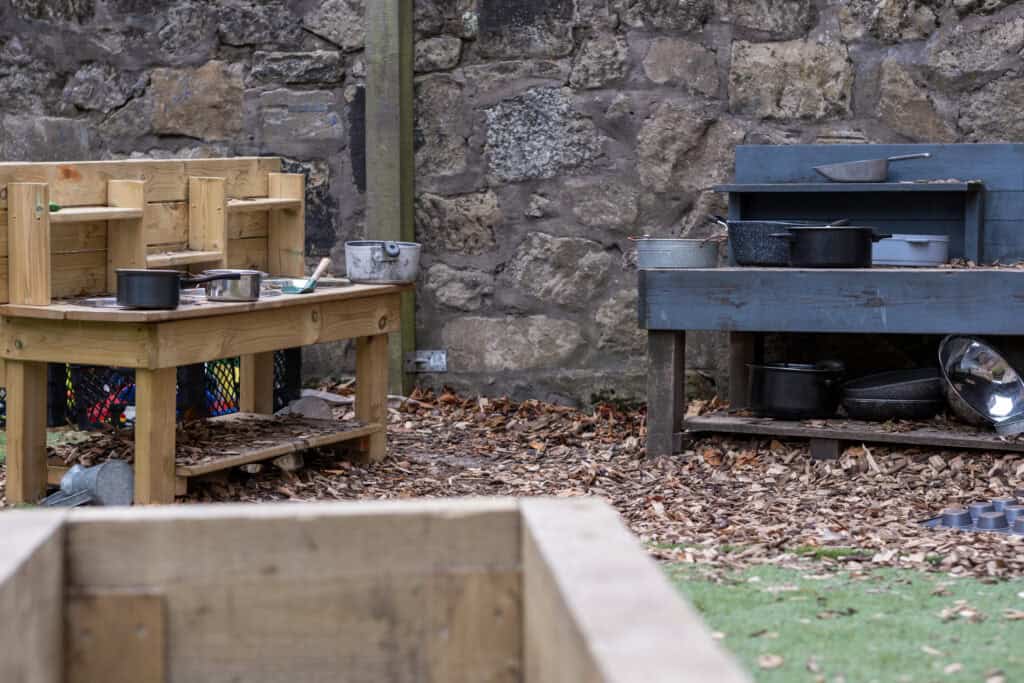 1. Outdoor play kitchen for children at Thrive Childcare, featuring wooden and blue play sets with toy cookware, suitable for early childhood development and imaginative play activities.