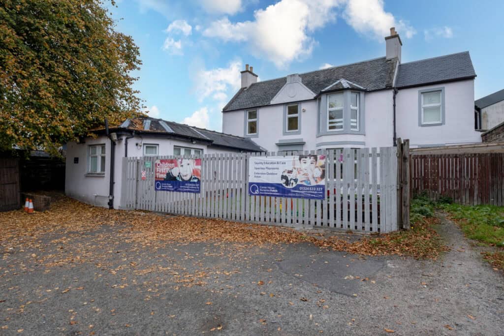 Bright white childcare nursery building with colourful signage, spacious outdoor play areas, and extensive outdoor spaces for children’s activities at Thrive Childcare, fostering learning and development.