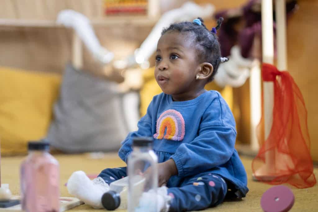 Bright young girl sitting on the floor engaged in imaginative play at Thrive Childcare, fostering early childhood development, creativity, and learning in a nurturing environment.