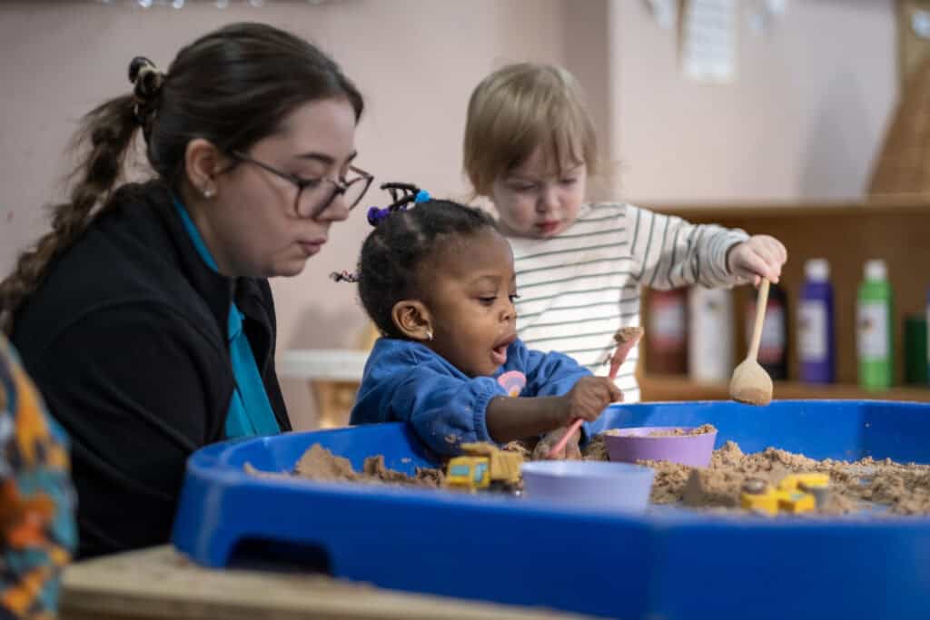 A young teacher engaging children in sensory play with sand at Thrive Childcare, promoting early childhood development, creativity, and social skills in a nurturing learning environment.