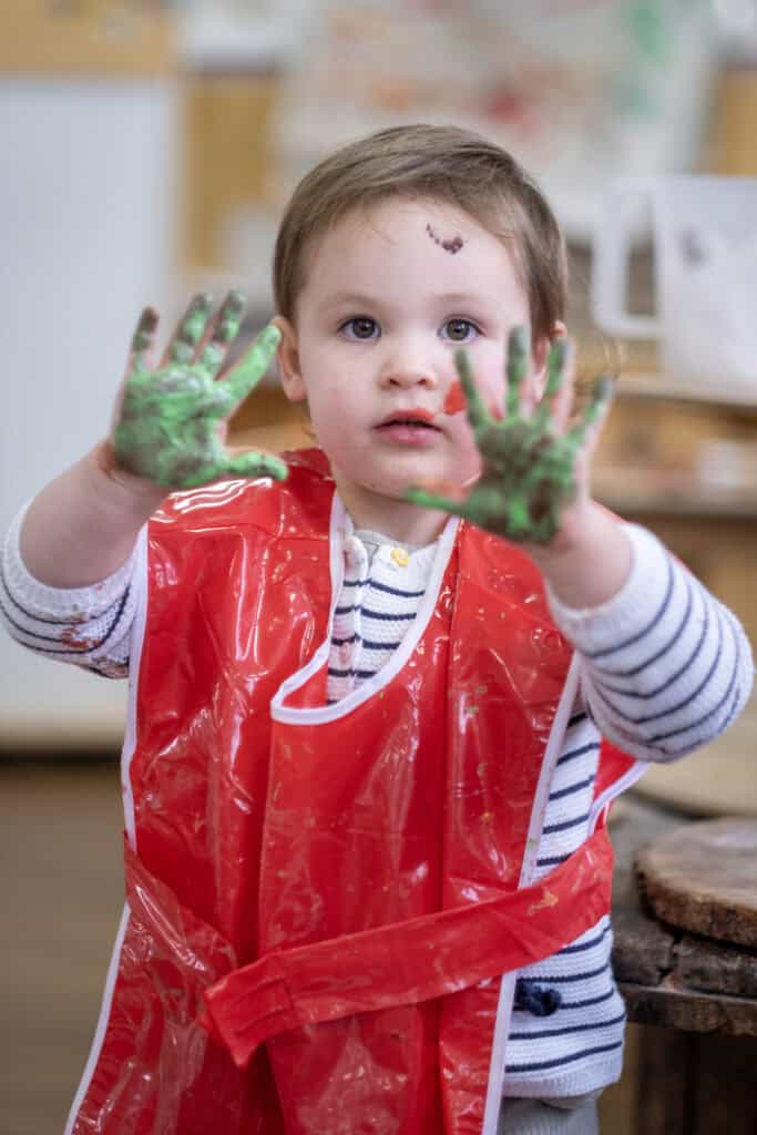 Bright young child with painted hands and face, enjoying creative art activity at Thrive Childcare. Engaging in colourful messy play in a nurturing learning environment.