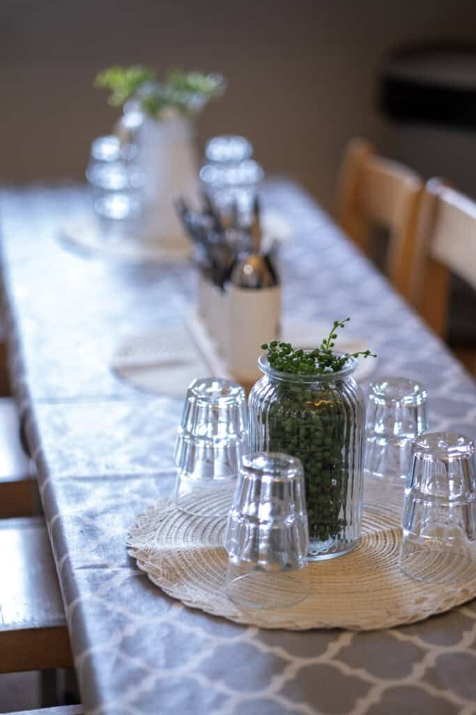 A clean, inviting dining table set for children at Thrive Childcare, featuring colourful glassware, a plant centrepiece, and a decorative tablecloth, promoting a welcoming environment for early childhood care.