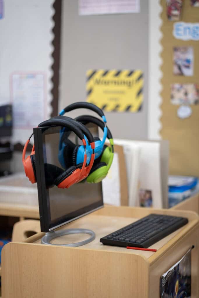 Headphones hanging on a computer monitor in a classroom, promoting engaging learning experiences at Thrive Childcare.