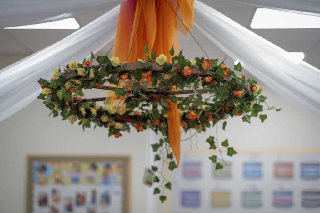 Vibrant ivy wreath with orange fabric and artificial flowers hanging in a colourful classroom at Thrive Childcare.