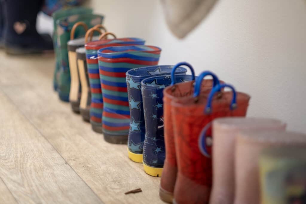 Brightly coloured children's rain boots lined up on a wooden floor at Thrive Childcare, promoting a fun and safe play environment for young children.