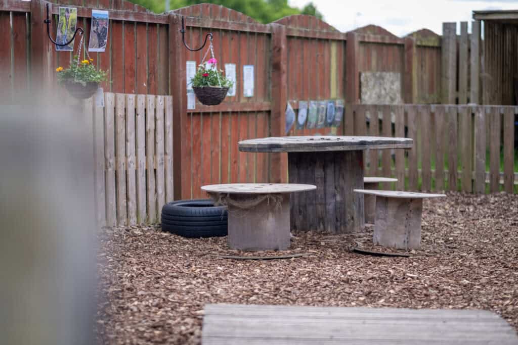Large outdoor wooden table and benches in a safe playground area at Thrive Childcare, promoting outdoor play, nature learning, and child's development in a caring environment.