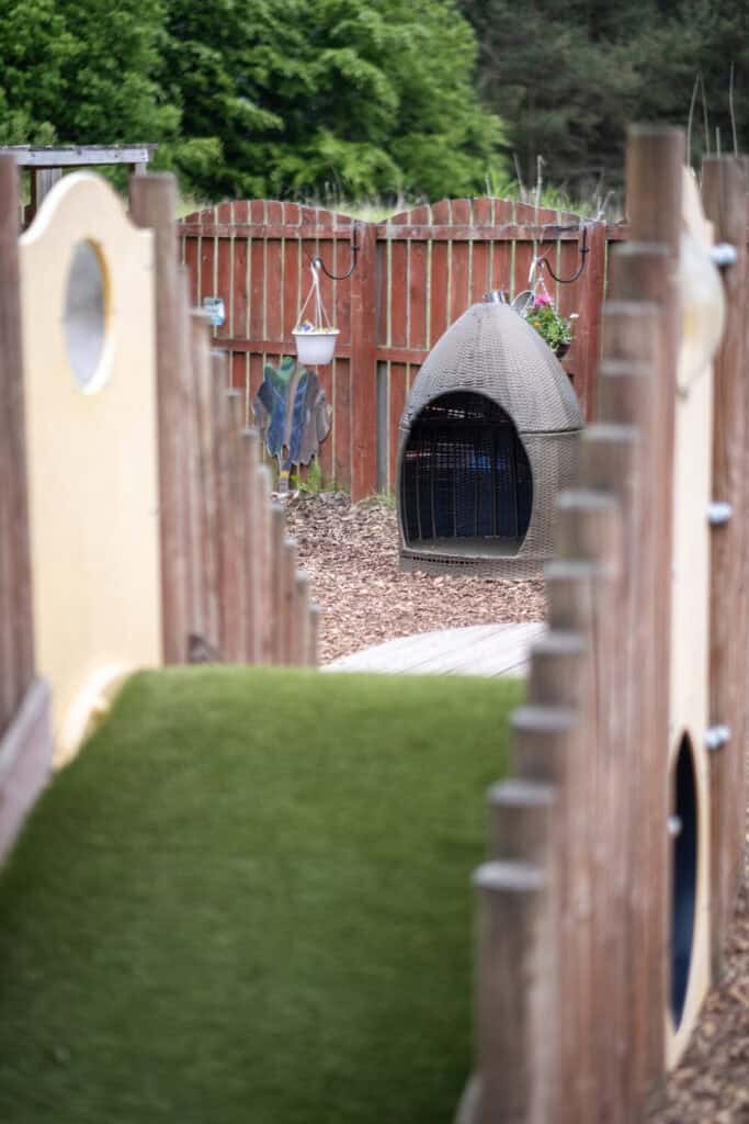1. Childcare outdoor play area with wooden fencing, climbing features, and a cosy dome-shaped shelter, ideal for early childhood development and outdoor learning.