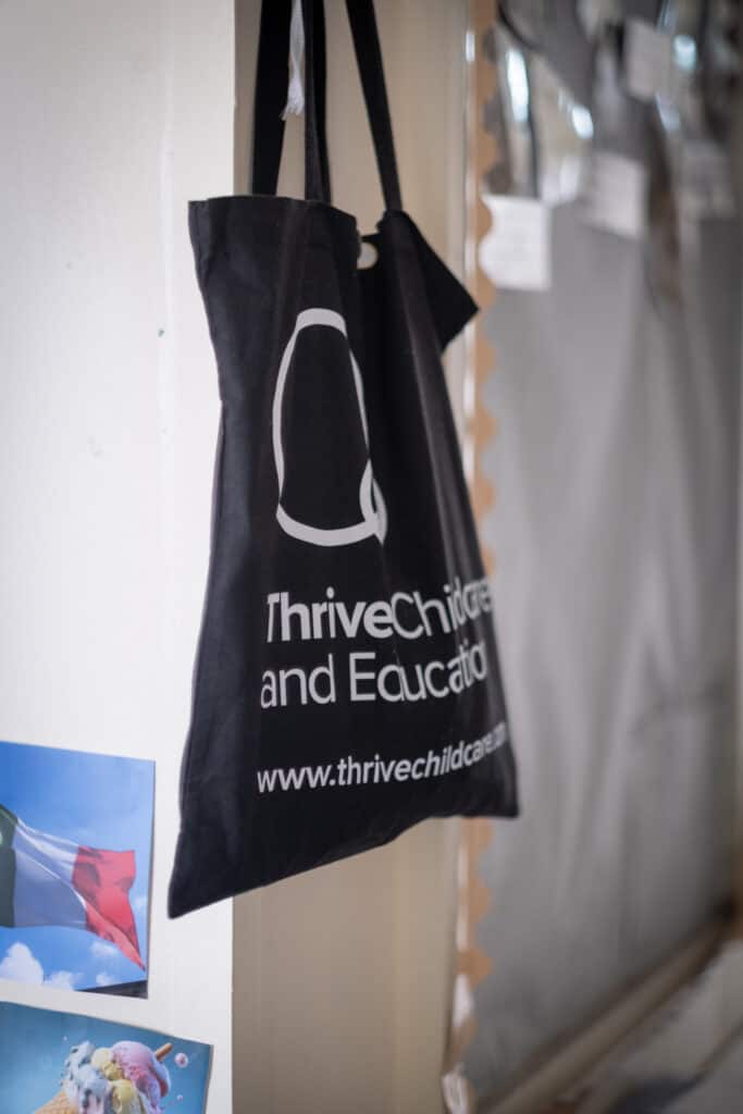 1. Recyclable black tote bag with Thrive Childcare branding hanging on a wall.