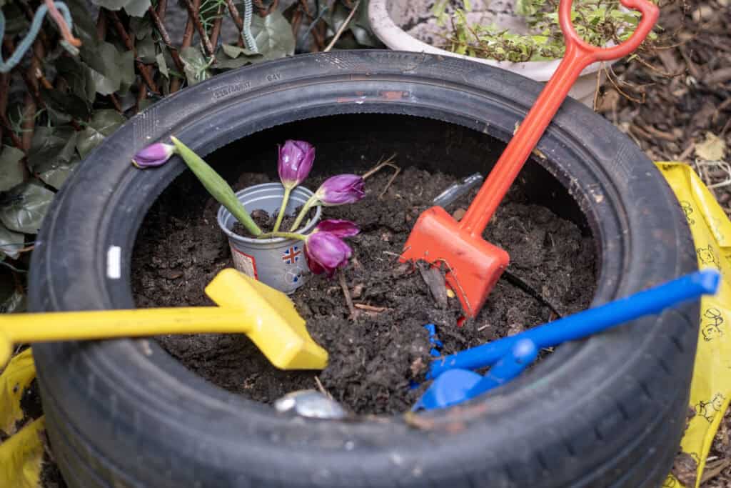 Brightly coloured children's shovels and a flower pot with purple tulips inside a recycled tyre garden bed, promoting outdoor learning and gardening activities at Thrive Childcare.