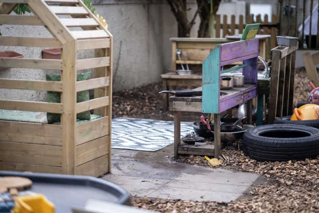Bright outdoor children's play kitchen area at Thrive Childcare, featuring wooden play structures and toy kitchen utensils for imaginative role play and outdoor fun.