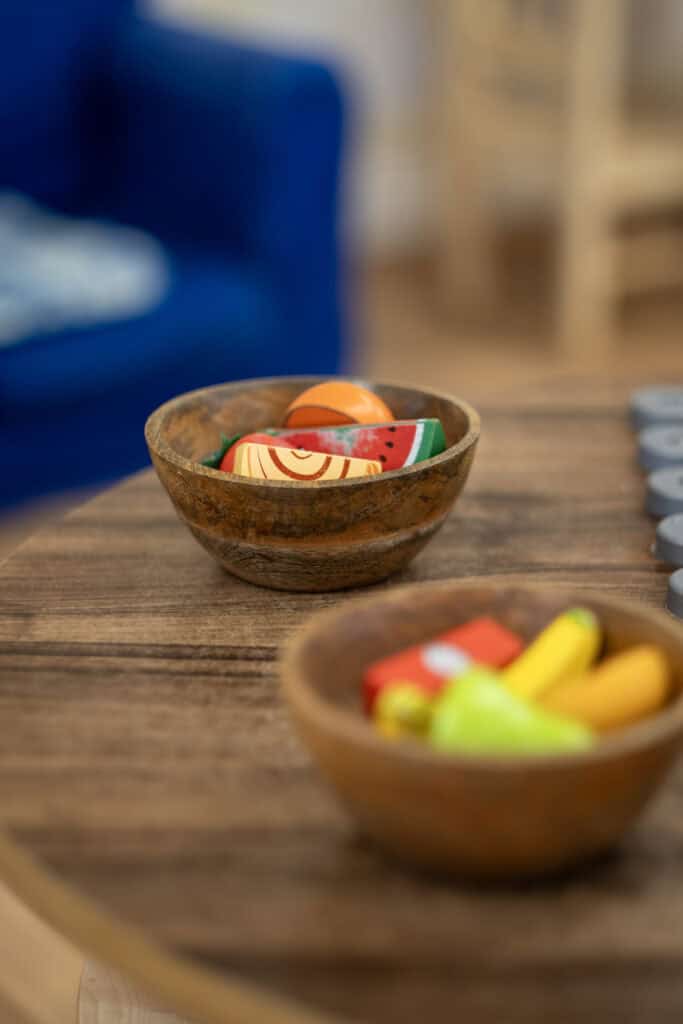 Colourful wooden toy food in bowls at Thrive Childcare play area.