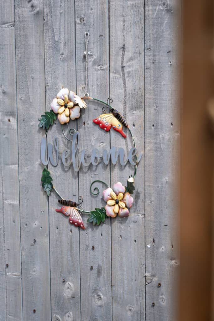 Bright colourful welcome sign with flowers and butterflies on a rustic wooden wall, reflecting a friendly and inviting atmosphere at Thrive Childcare.