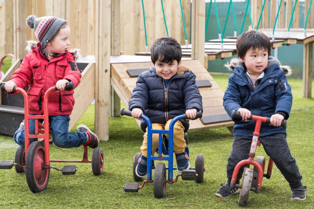 Young children playing on tricycles outdoors at Thrive Childcare, offering a safe and engaging environment for early childhood development and preschool activities.