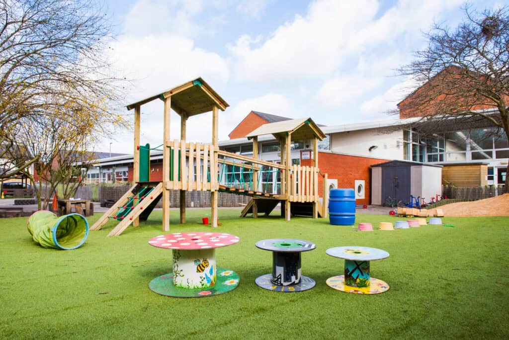 Bright outdoor play area with wooden playground structures, colourful tables, and sensory tunnels at Thrive Childcare, promoting early childhood development and safe outdoor fun for young children.