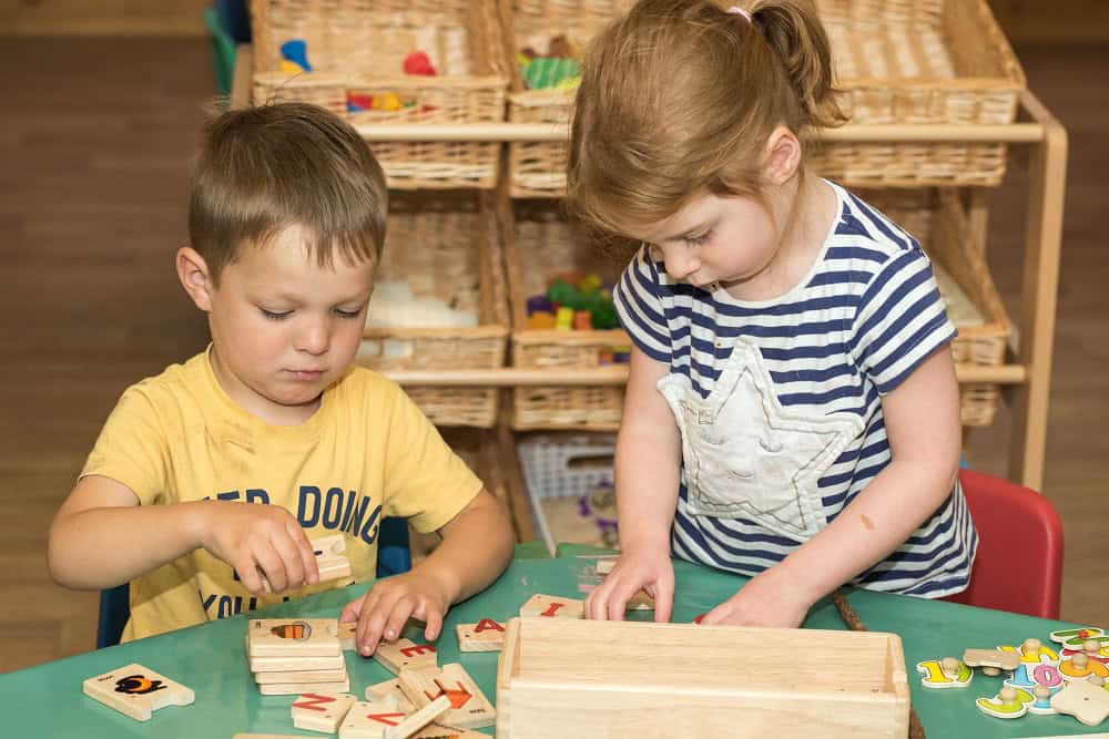 Engaging children playing with educational wooden alphabet puzzle at Thrive Childcare, promoting early learning and child development in a nurturing environment.