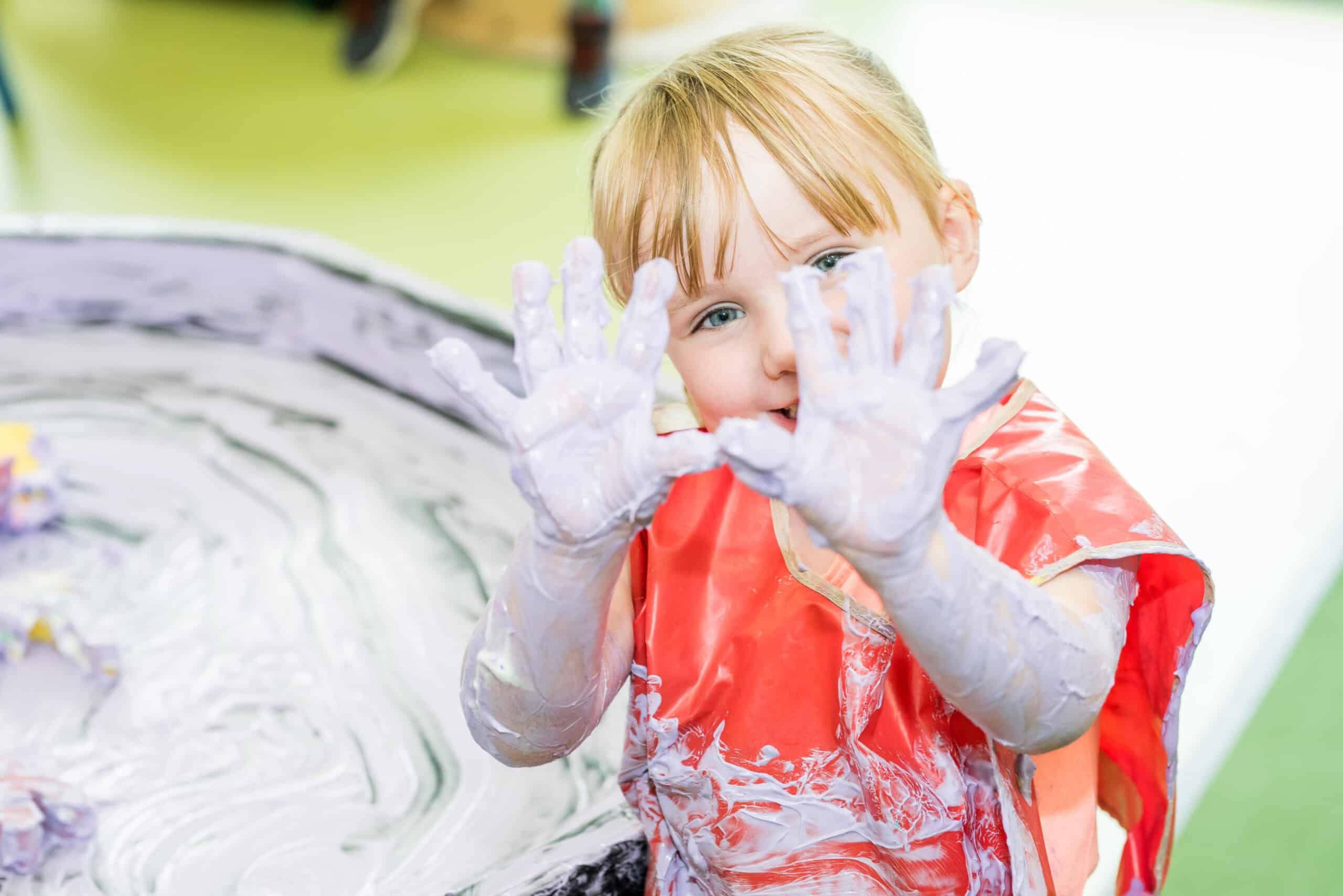 Bright red-haired child with blue eyes playing with finger paint at Thrive Childcare, engaging in creative early childhood development activities in a nurturing environment.