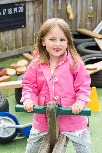 Smiling young girl playing outdoors on playground equipment at Thrive Childcare, promoting fun and safe early childhood development.