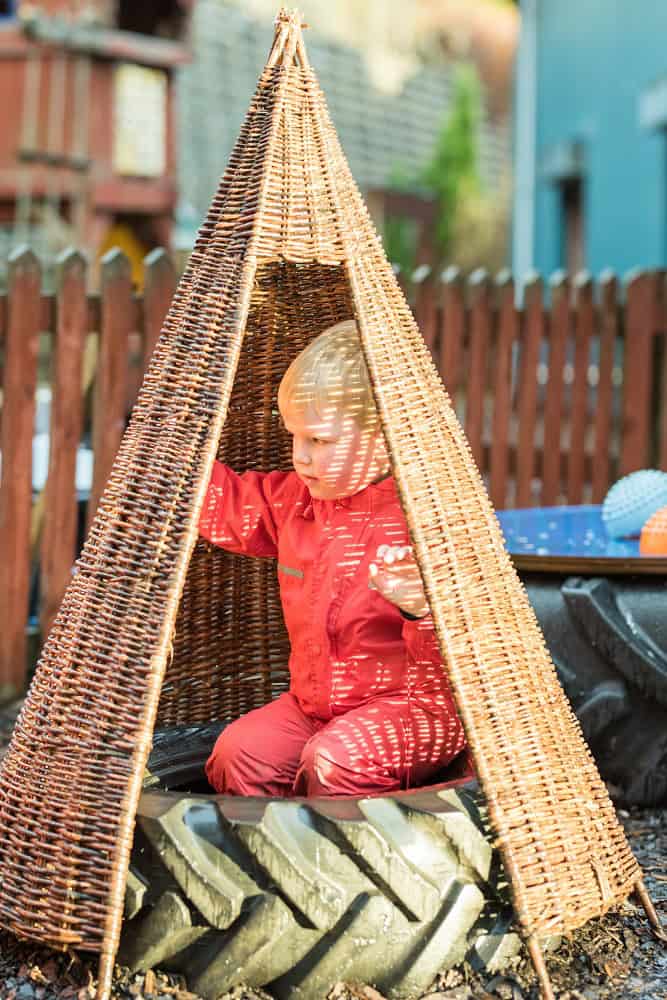 Children's outdoor play at Thrive Childcare featuring a children’s play tent made of wicker and imaginative fun. Safe, engaging environment for early childhood development and outdoor recreation.