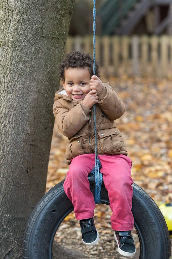 Bright smiling child on tire swing in outdoor playground, enjoying nature and play at Thrive Childcare, offering a safe environment for child development, fun activities, and early learning experiences.