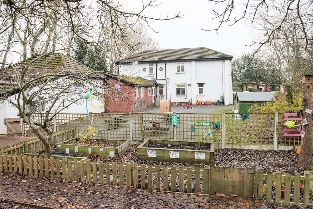 A welcoming outdoor play area at Thrive Childcare, featuring garden beds, colourful decorations, and a secure fence, designed to promote early childhood development and outdoor learning.