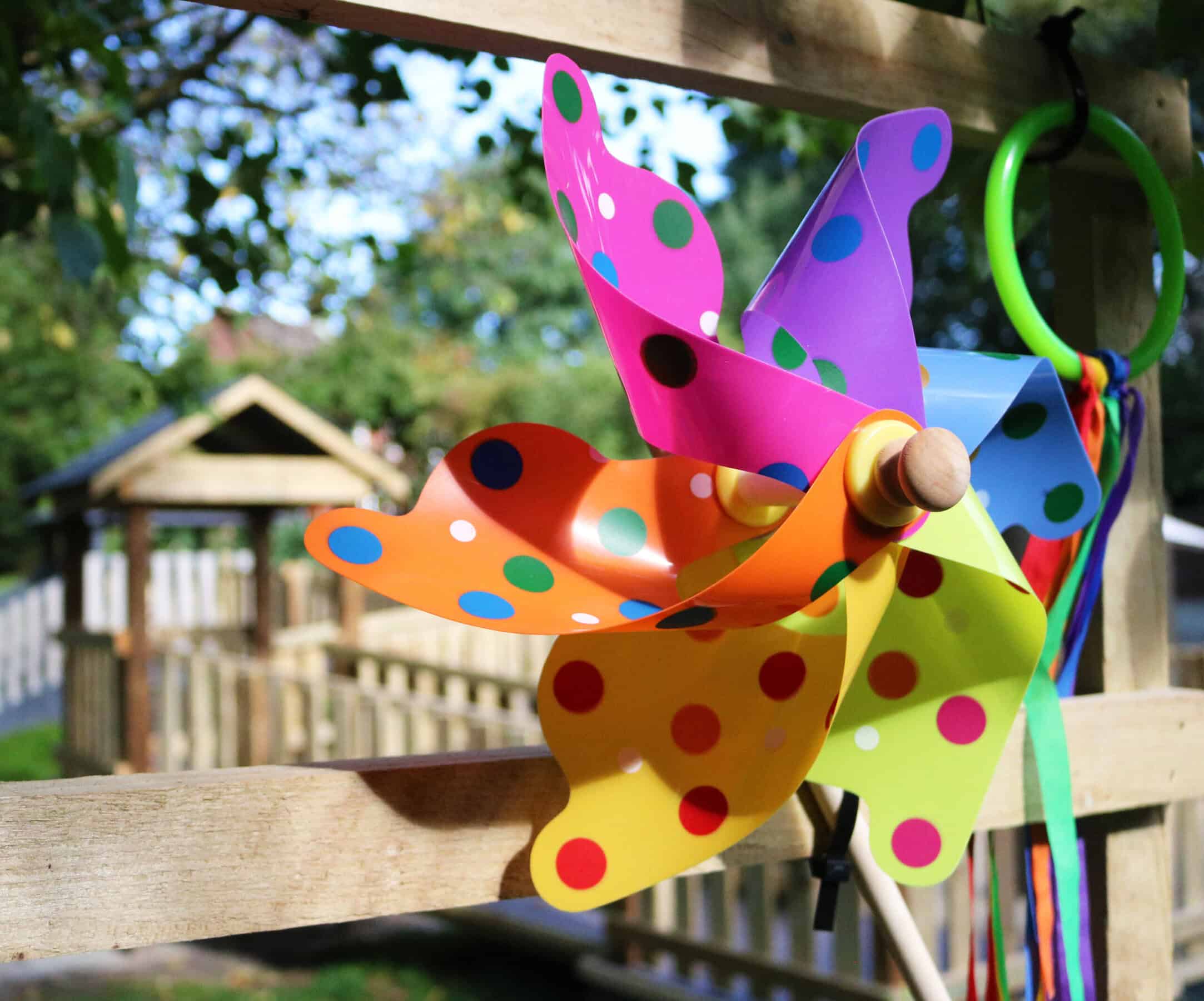 Brightly coloured polka dot pinwheel on a wooden fence at Thrive Childcare outdoor play area, highlighting fun and engaging outdoor activities for children.