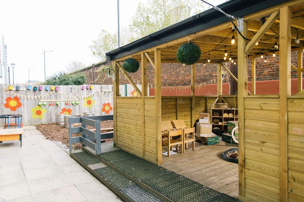 Bright outdoor childcare area with wooden play structures, colourful wall decorations, and protected shaded play space at Thrive Childcare.