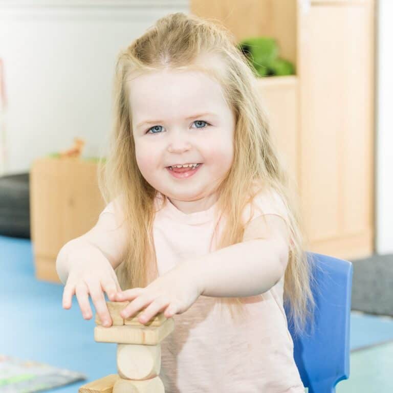Bright happy preschool girl playing with wooden blocks at Thrive Childcare, a trusted early childhood education centre.