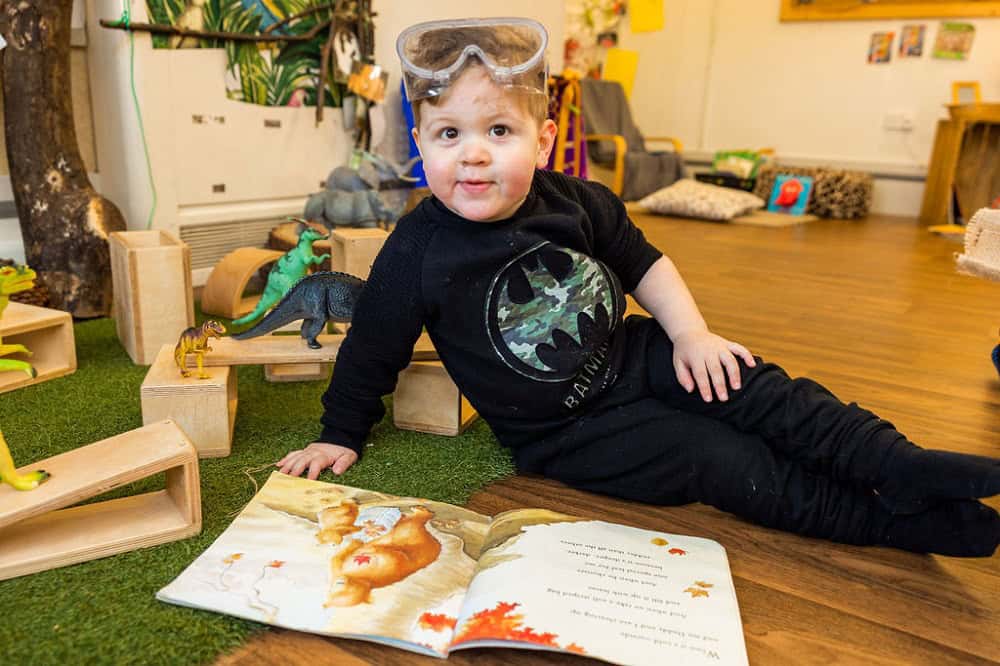 Young child playing with toys and reading a picture book at Thrive Childcare, inspiring early childhood learning and development in a nurturing environment.