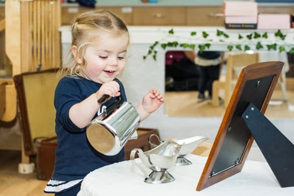 Young girl engaging in pretend play, pouring tea at a virtual classroom activity in a caring childcare environment.