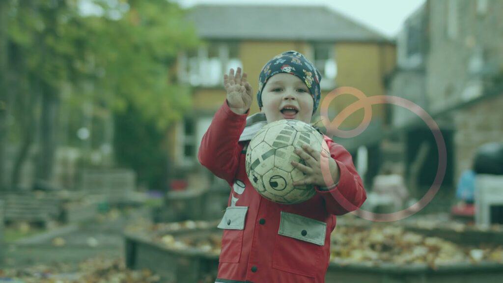 A young child holding a soccer ball and waving, playing outdoors at Thrive Childcare, highlighting early childhood activities, play, and development in a safe, nurturing environment.