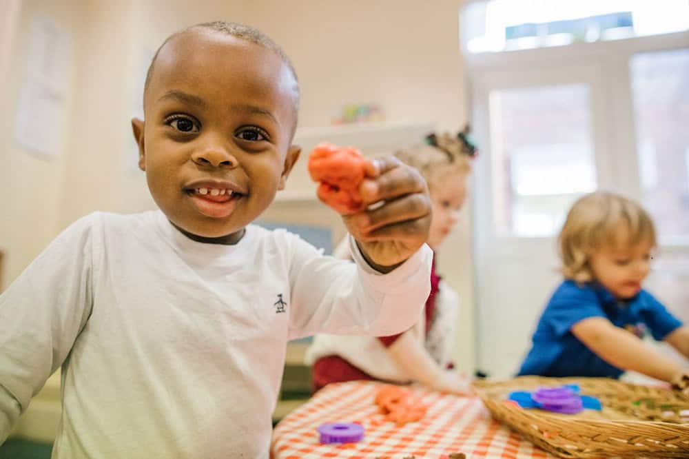 Bright young child smiling and holding colourful play dough at Thrive Childcare preschool, supporting early childhood development, creativity, and engaging learning activities.