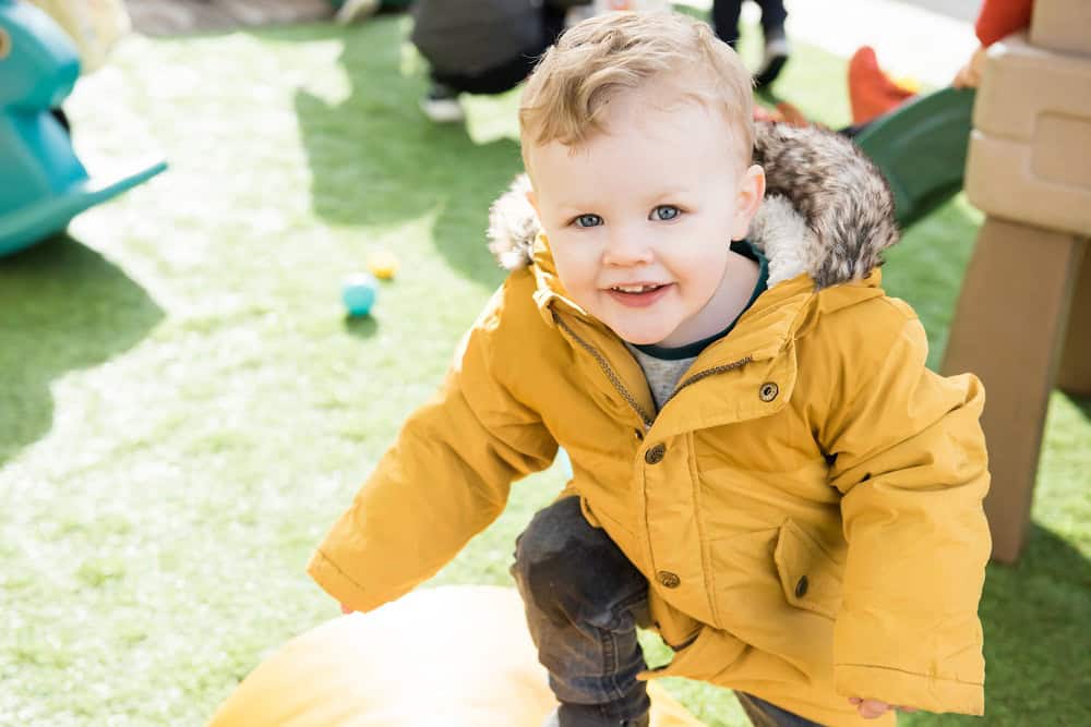 Bright young child in a yellow jacket enjoying outdoor play at Thrive Childcare, emphasising early childhood development and outdoor activities.
