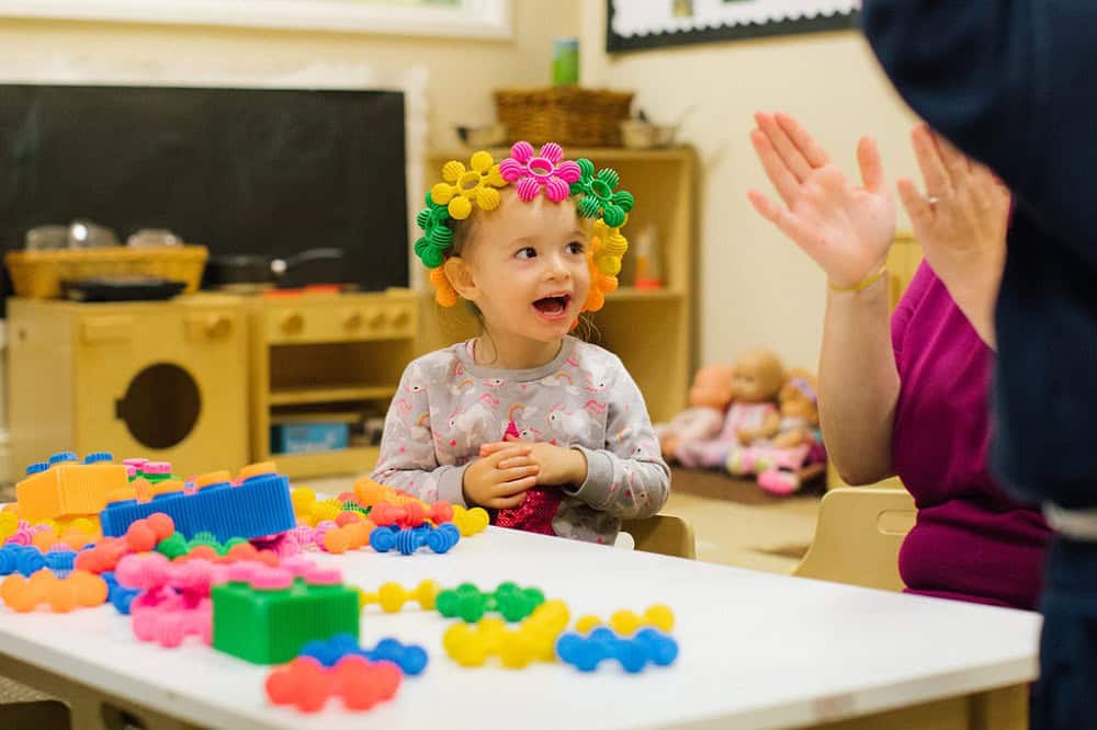 Bright-topped child engaging with a teacher during playtime at Thrive Childcare in a colourful classroom setting, promoting early childhood education and social development.