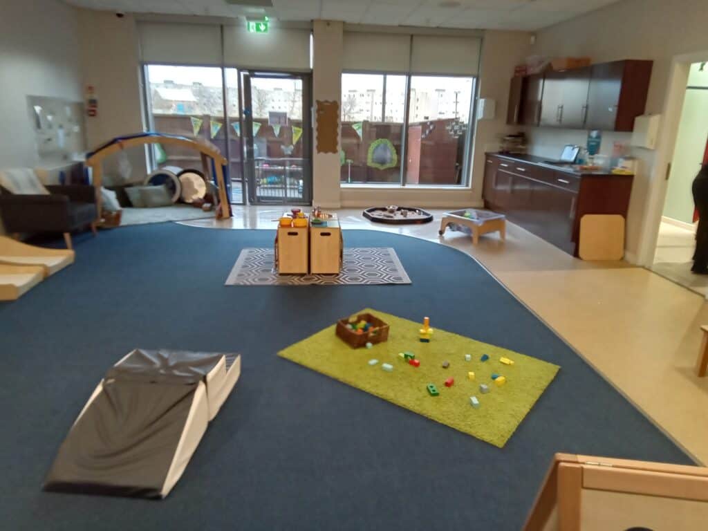 Bright indoor childcare playroom with soft carpets, educational toys, and natural light; perfect for engaging early childhood development at Thrive Childcare.