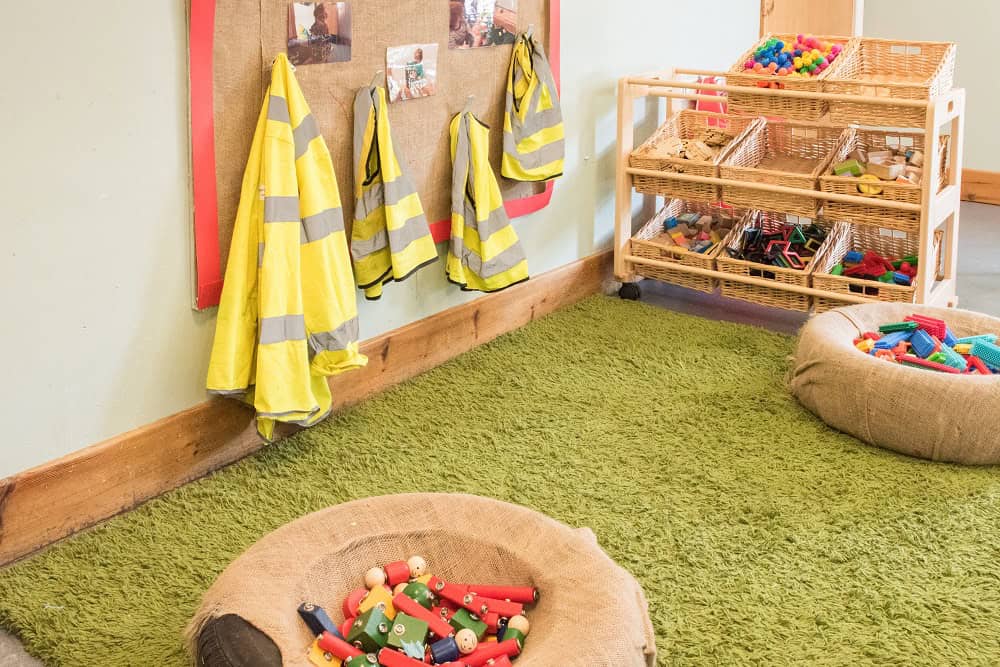 Brightly lit classroom with toy storage, safety jackets hung on the wall, and soft play mats, creating a safe, engaging environment for children at Thrive Childcare, promoting early childhood development and play.
