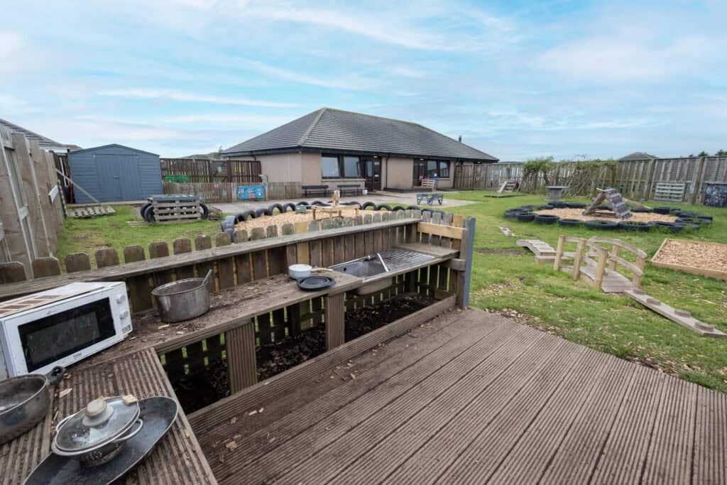 Bright outdoor childcare play area at Thrive Childcare with soft grass, wooden ramps, sandboxes, and sensory zones, ideal for children’s learning and development.