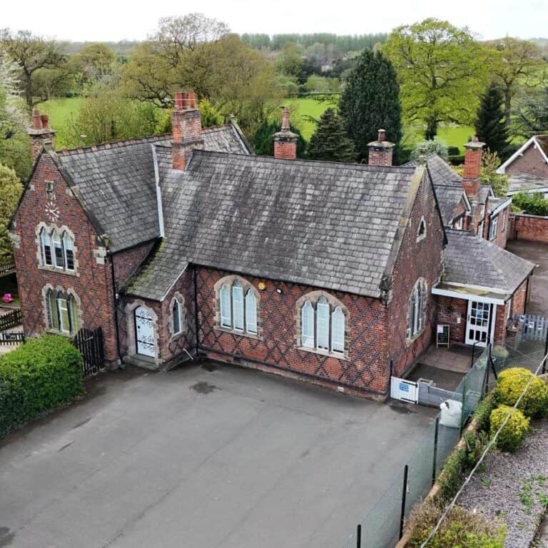 Bright red brick building with pitched roof, tall chimney pots, and arched windows, surrounded by greenery; ideal for childcare or community use.