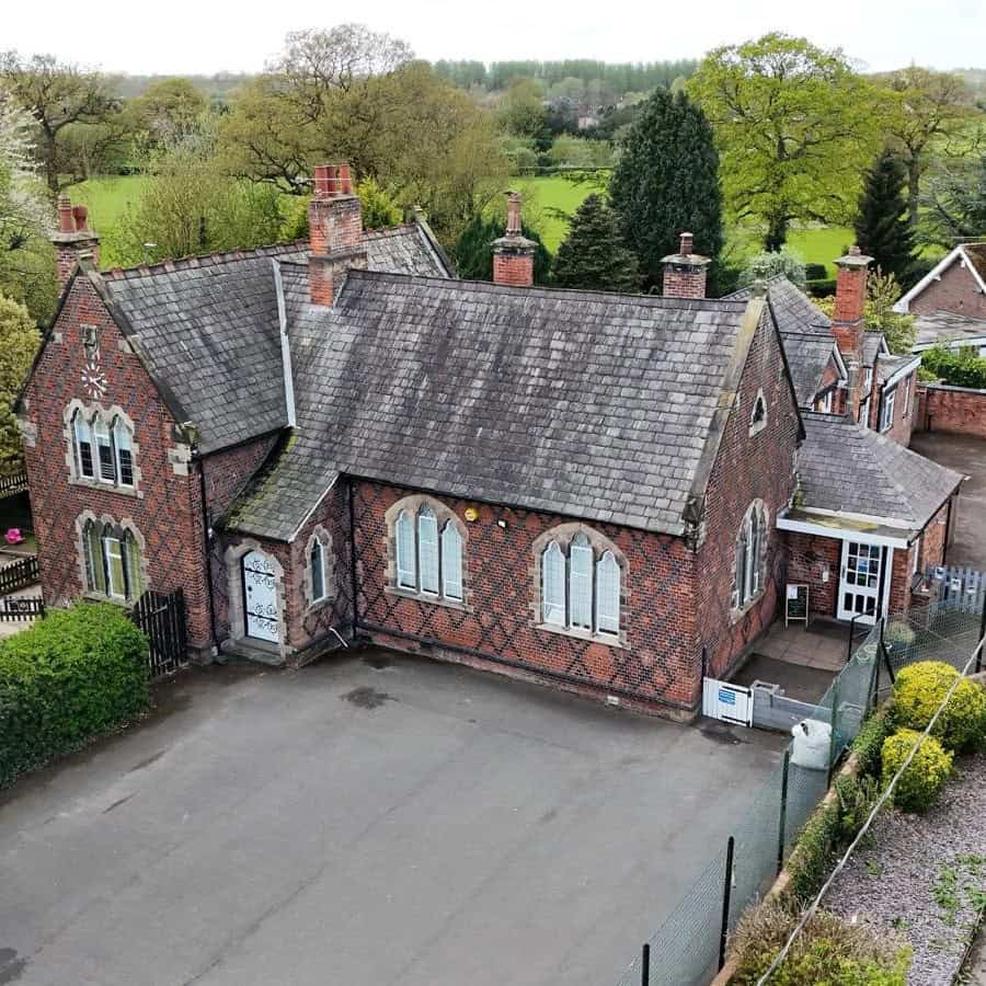 Bright red brick building with pitched roof, tall chimney pots, and arched windows, surrounded by greenery; ideal for childcare or community use.