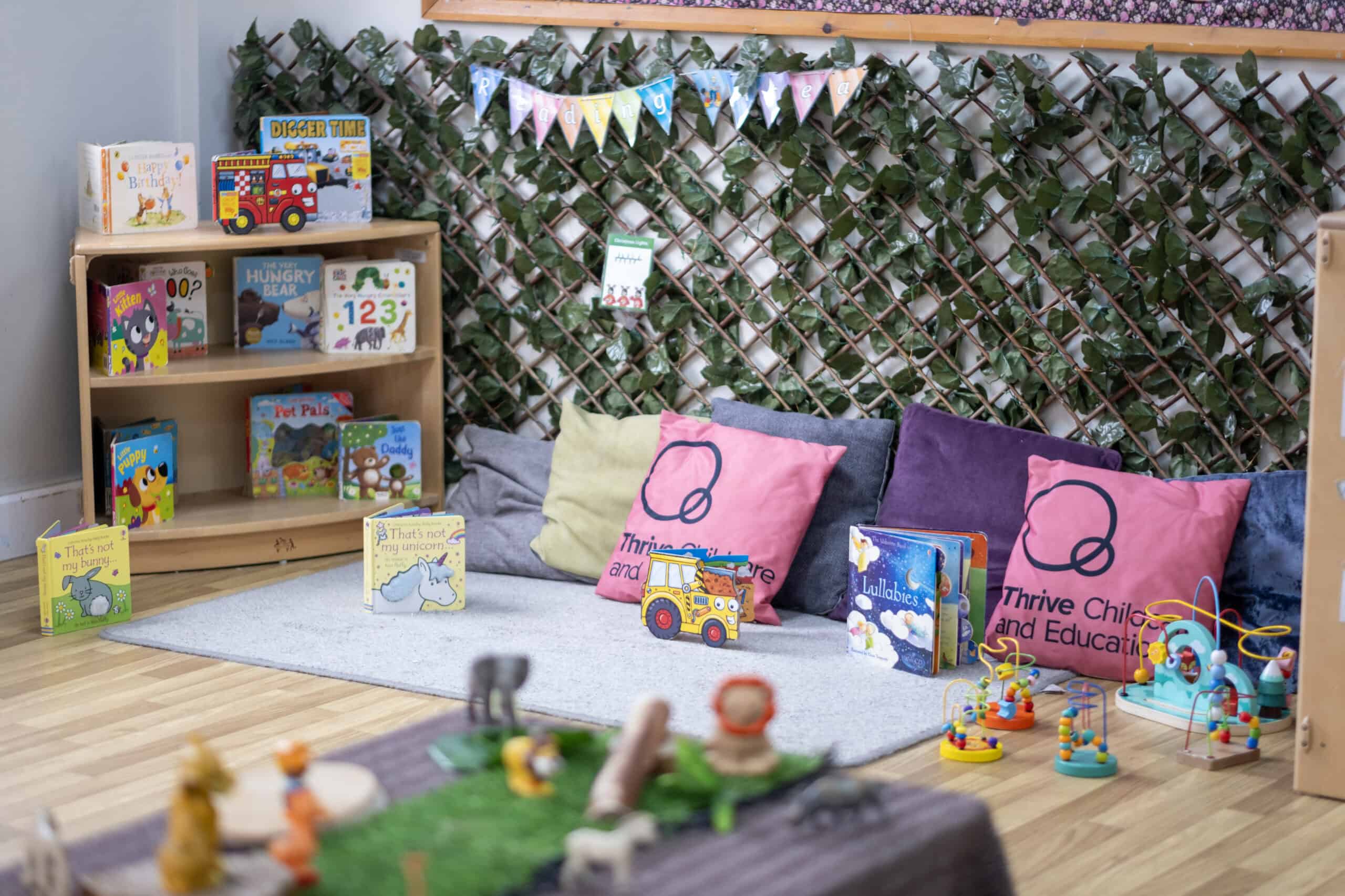 Bright nursery reading corner with colourful children's books, cushions, and soft toys, fostering learning and comfort at Thrive Childcare and Education. A cozy space for young learners to explore.
