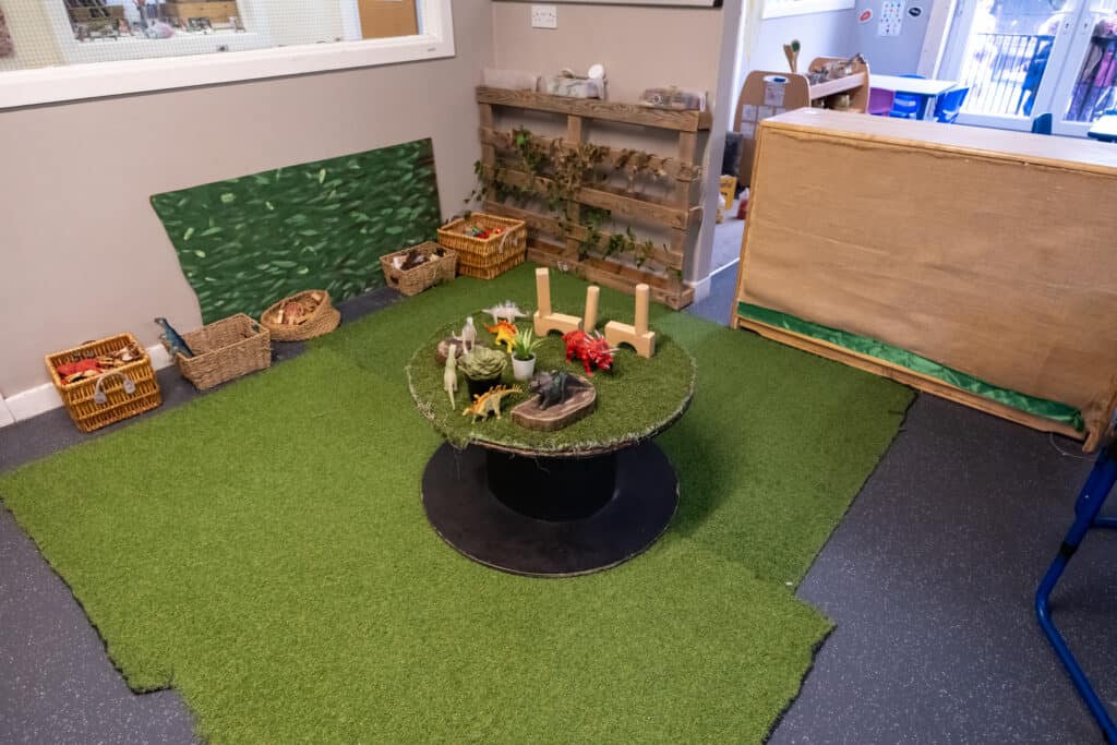 Bright indoor play area at Thrive Childcare with dinosaur toys, natural-themed decor, and a grassy area for imaginative activities, promoting early childhood development and play-based learning.