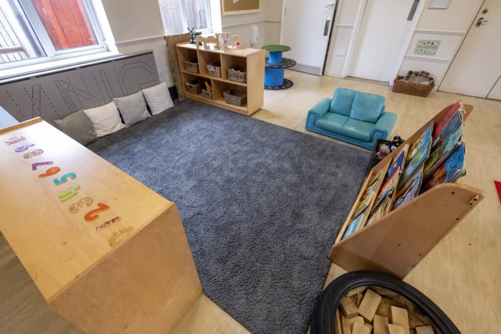Bright early childhood learning room with soft grey rug, colourful educational toys, and cozy seating areas, designed for infants and toddlers at Thrive Childcare, creating a safe and stimulating environment.