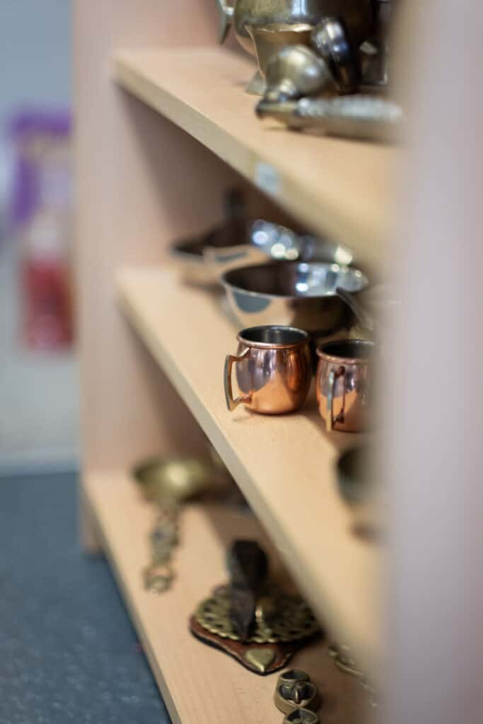 Polished metal cups on wooden shelves at Thrive Childcare, showcasing a warm, welcoming environment with kitchen and play area essentials for children’s daily needs.