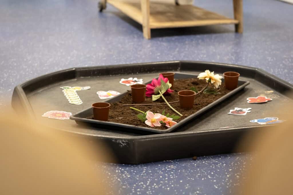 Brightly decorated flower planting activity with paper stickers and small flower pots, encouraging early childhood development and creativity at Thrive Childcare.