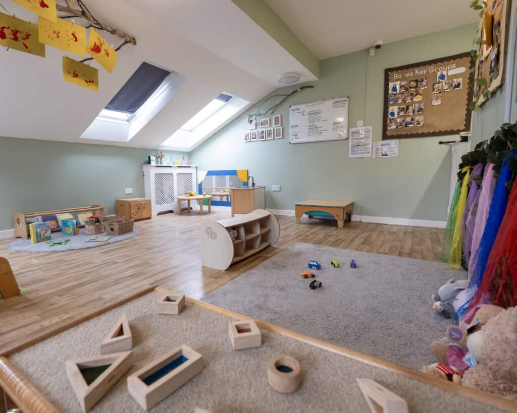 Bright and inviting childcare room with natural light, wooden toys, colourful curtains, and educational displays, providing a safe and stimulating environment for young children’s play and learning.