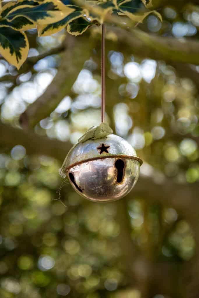 A children's garden bell with a frog on top, hanging among lush greenery for outdoor play and learning. Perfect for early childhood development and nature-based childcare activities.