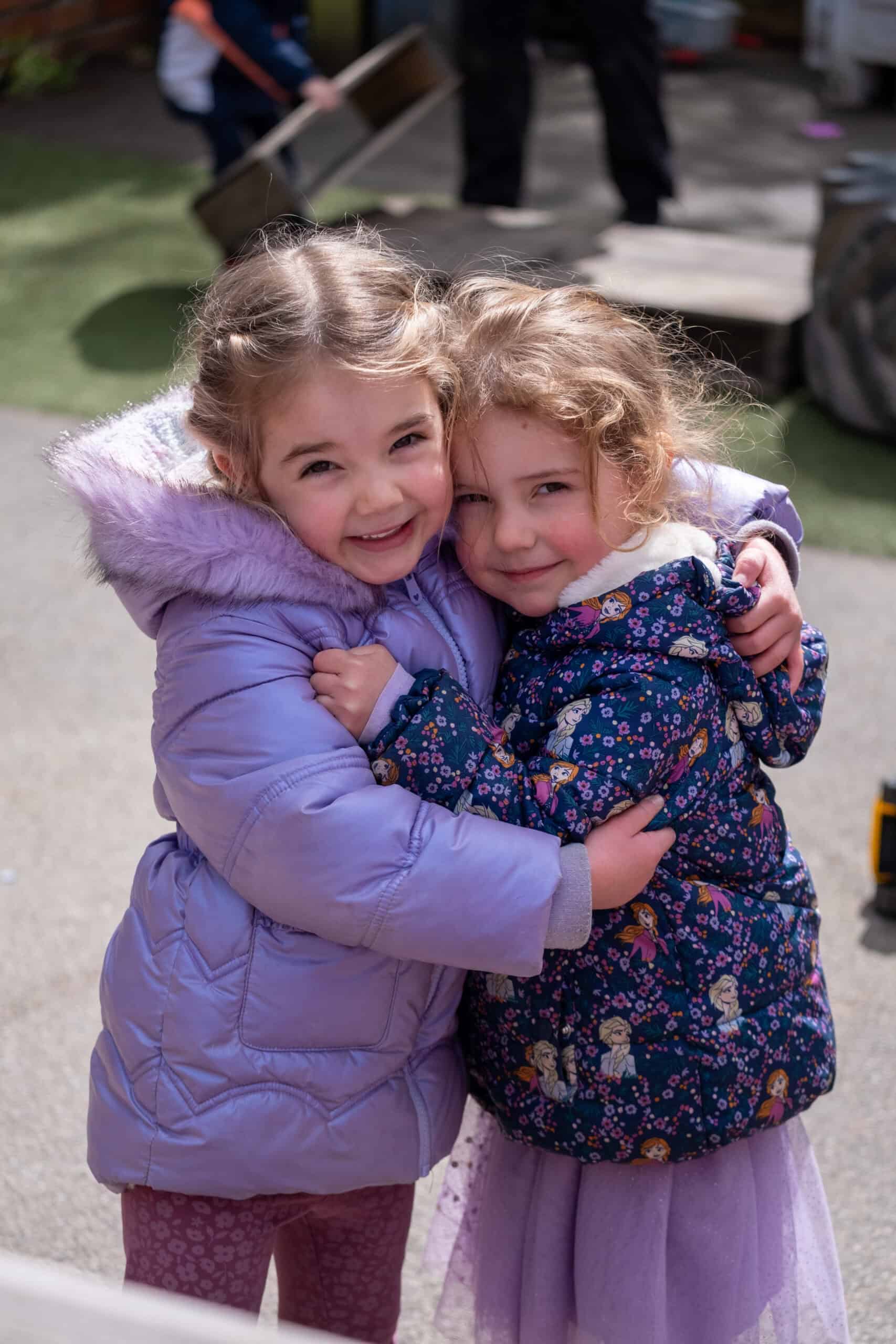 Cheerful young girls hugging outdoors at Thrive Childcare, showcasing happy children in a caring early childhood education environment.