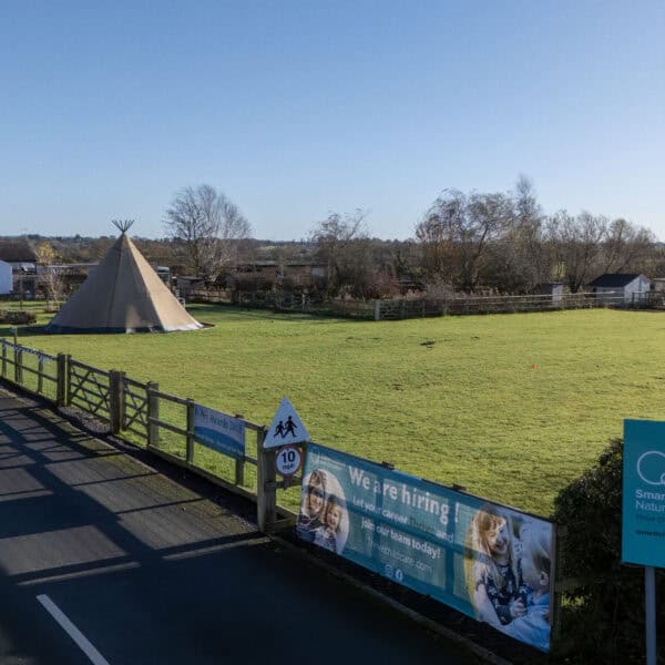 Bright, spacious outdoor play area at Thrive Childcare, featuring a tipi, lush green grass, and supporting early childhood education and childcare services in a safe environment.