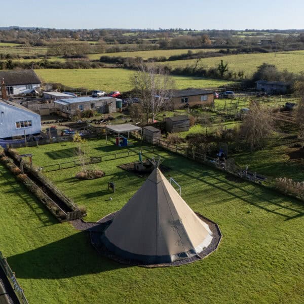 Colourful outdoor childcare play area at Thrive Childcare with tipi, trees, and fenced garden for early childhood development and outdoor learning.