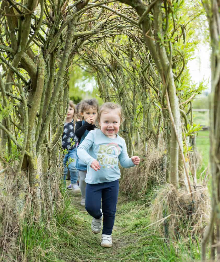 1. Children exploring a natural woodland tunnel at Thrive Childcare, fostering outdoor learning and play in a safe, nurturing environment for early childhood development.