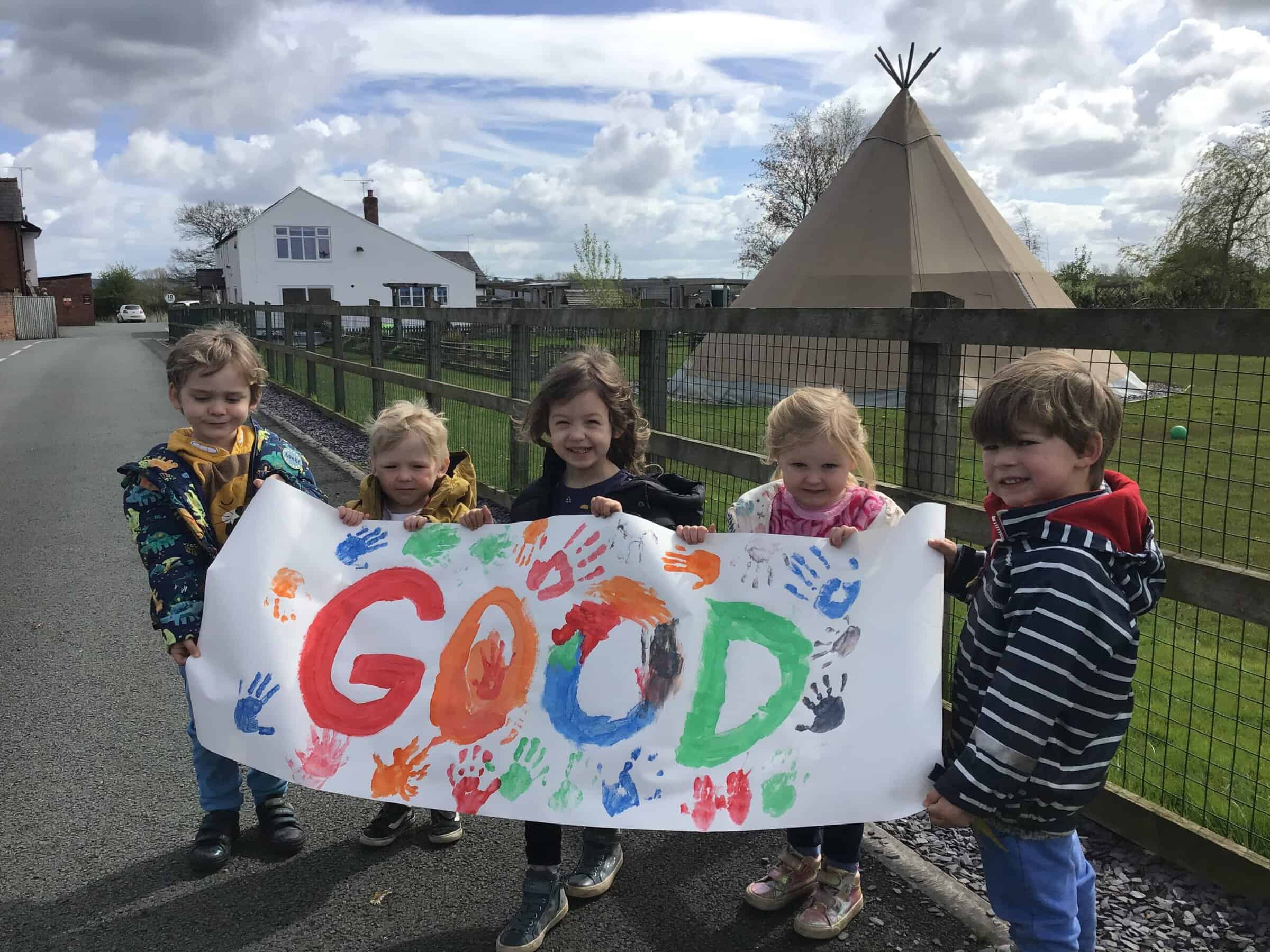 Brightly coloured children holding a "GOD" banner with handprint decorations outside at Thrive Childcare, showcasing a happy, engaging childcare environment in a safe outdoor space.